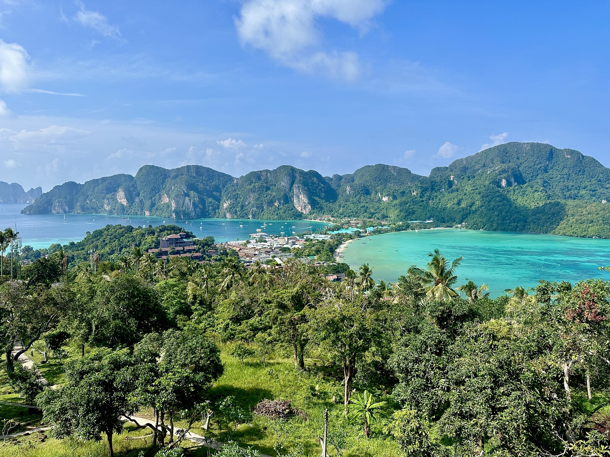 A panoramic view of Koh Phi Phi, Thailand, showcasing lush green hills, turquoise waters, and a serene bay with boats.