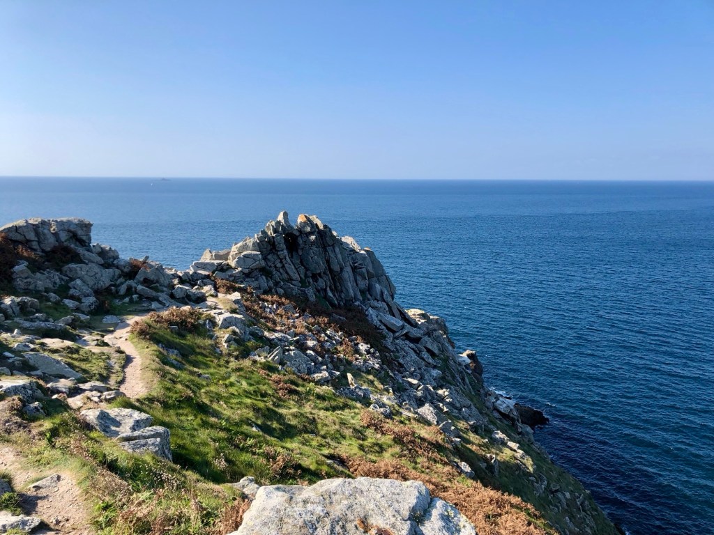 Vue panoramique sur la côte de Bretagne avec des rochers surplombant l'océan Atlantique et un ciel bleu dégagé.