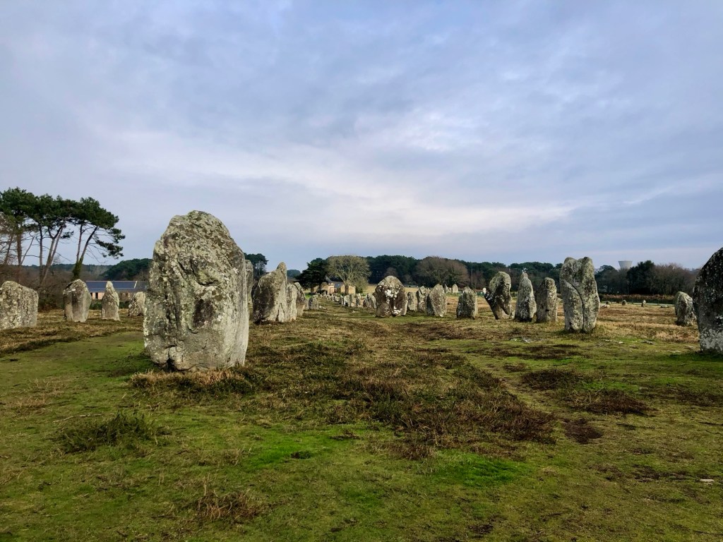 Alignement de menhirs à Carnac, Bretagne, avec des pierres taillées et un ciel nuageux en arrière-plan.